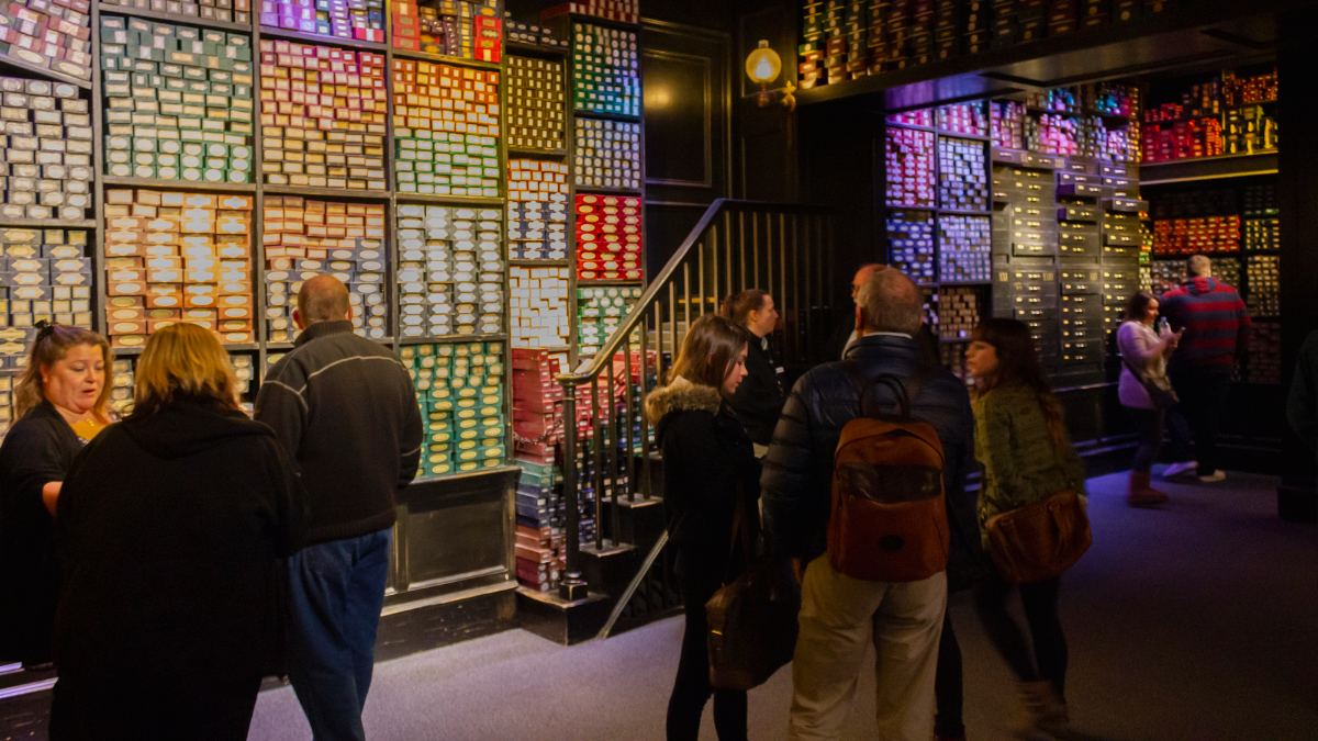 Pareti di scatole di bacchette colorate nel negozio degli studi di Harry Potter, con i visitatori tra gli scaffali
